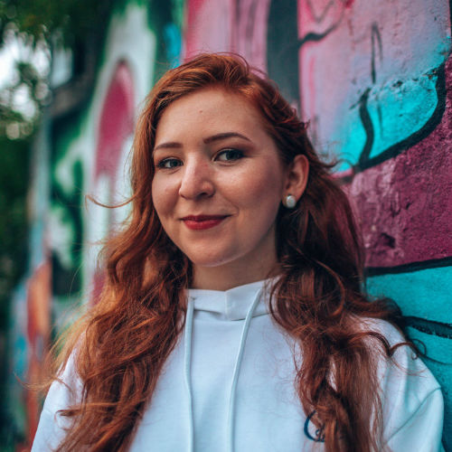 A woman standing in front of a colourful graffitied wall.